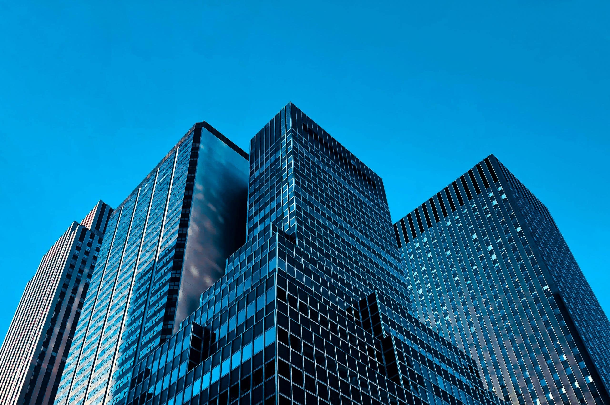 A low-angle view of several modern skyscrapers with reflective glass windows against a clear blue sky